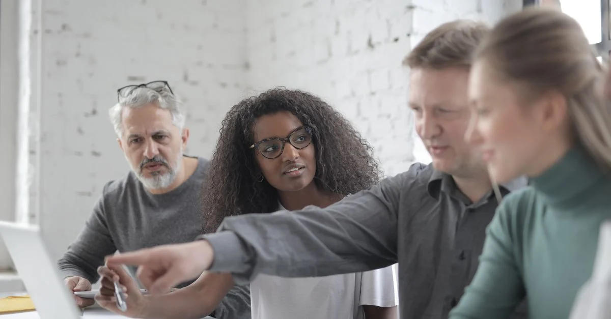 Un groupe diversifié de professionnels dans un bureau moderne discutant d'un projet autour d'un ordinateur portable.