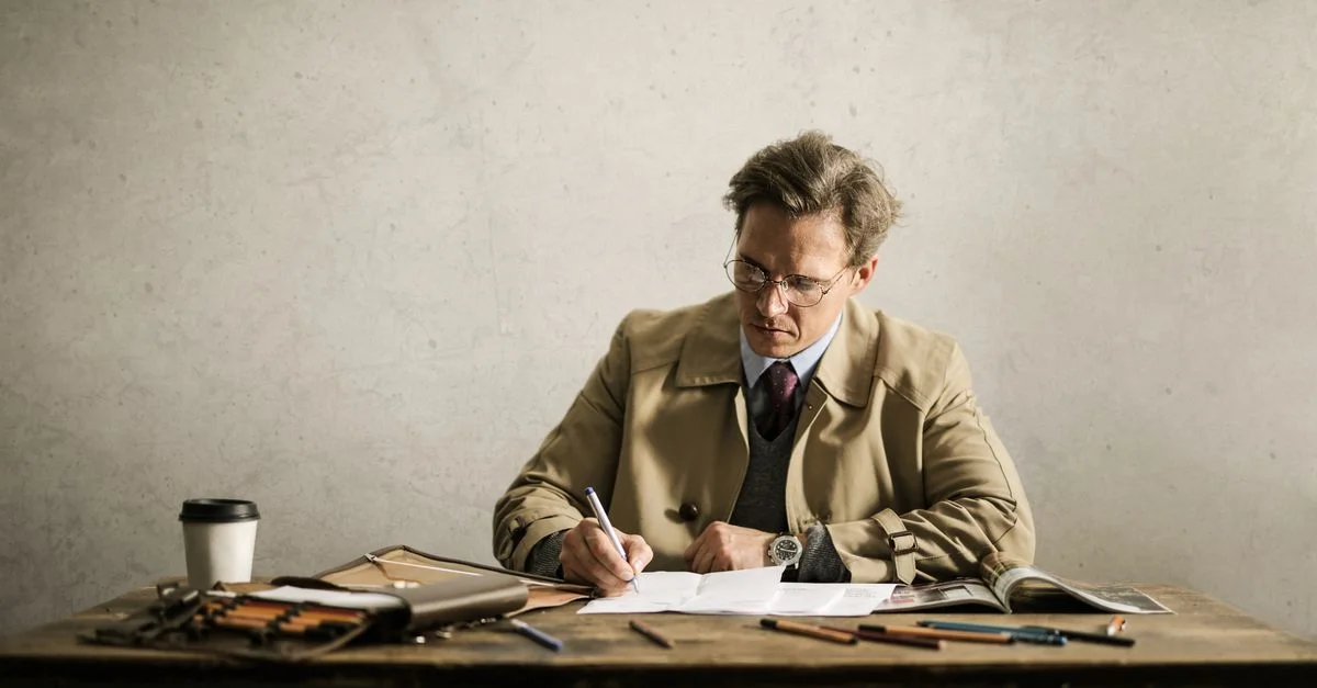 Un professionnel masculin en manteau beige concentré sur des documents à son bureau.