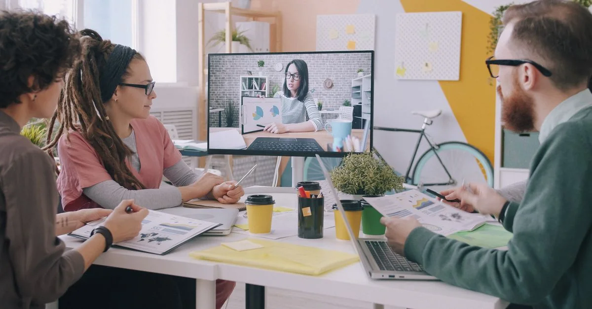 Une équipe créative, dans un bureau moderne, participe à une réunion par vidéoconférence pour discuter de stratégies commerciales.
