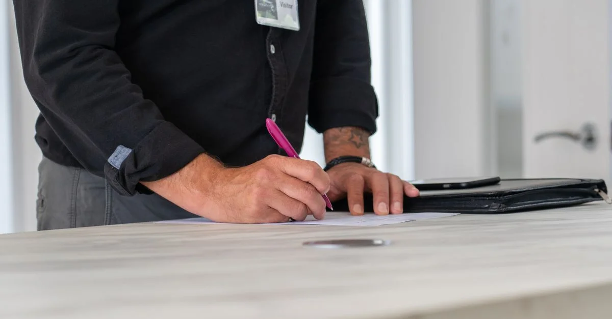Un homme d'affaires signe des documents à un bureau moderne, l'accent étant mis sur ses mains et son espace de travail.