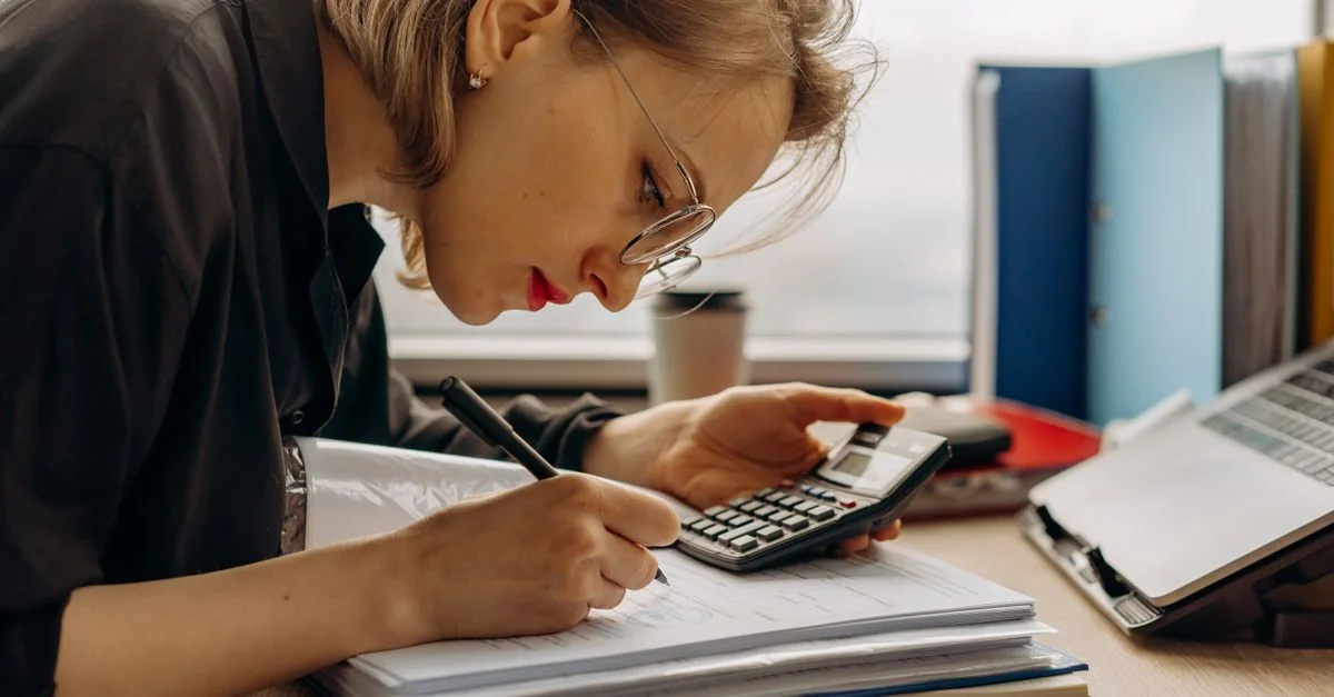 Jeune femme travaillant assidûment sur la comptabilité avec une calculatrice et des documents. Parfait pour des thèmes d'affaires et de finance.
