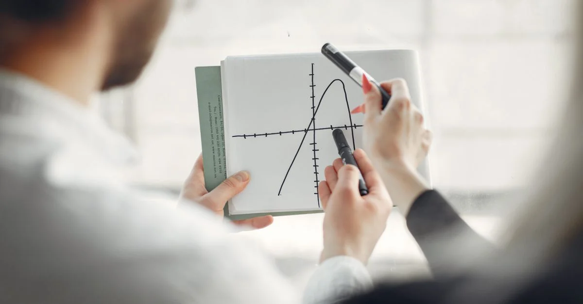 Deux professionnels discutant d'un graphique de parabole sur un carnet, favorisant le travail d'équipe et la collaboration.
