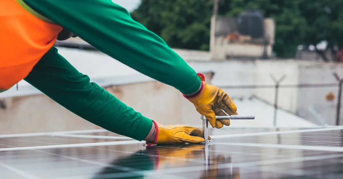 Un technicien solaire travaillant sur l'installation de panneaux solaires sur un toit, avec un accent sur les outils et l'équipement de sécurité.