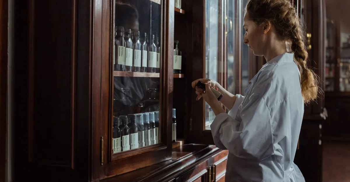 Une pharmacienne en uniforme blanc organisant des bouteilles dans un cabinet de pharmacie.