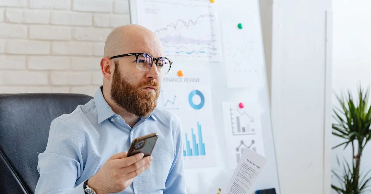 Homme chauve avec des lunettes examine des données financières dans un bureau avec des diagrammes.