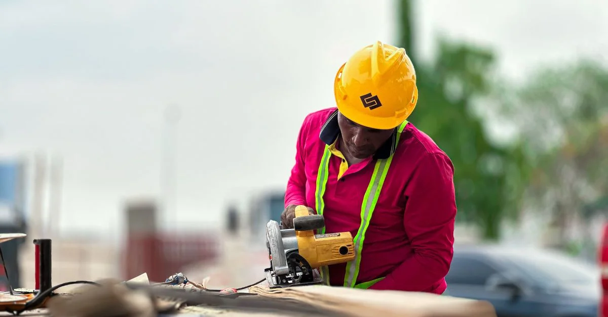 Ouvrier du bâtiment portant un équipement de sécurité utilisant une meuleuse d'angle sur un site en extérieur.