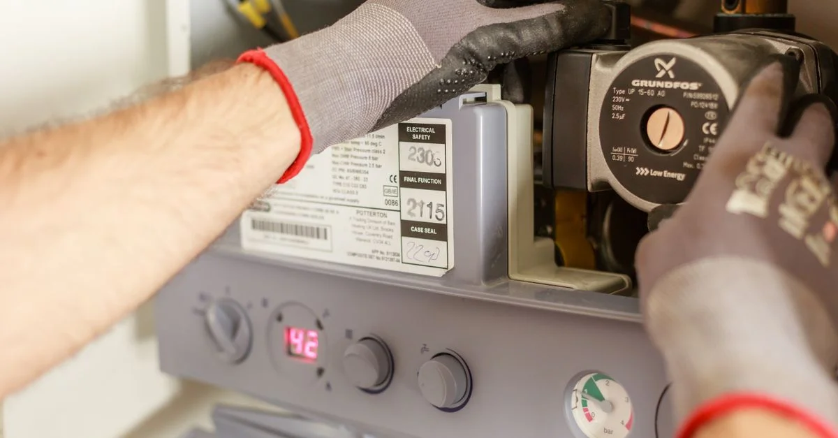 Gros plan sur des mains ajustant un système de chaudière avec des instruments précis, montrant un travail d'entretien.